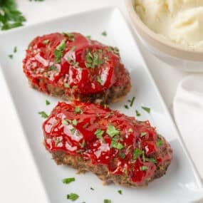 Mini meatloaf recipe served with mashed potatoes and topped with a glossy ketchup glaze.
