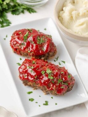 Mini meatloaf recipe served with mashed potatoes and topped with a glossy ketchup glaze.