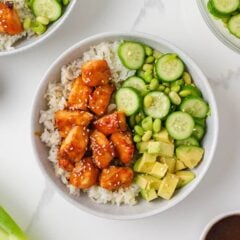 Teriyaki salmon rice bowl with cucumber, edamame, avocado, green onions and sesame seeds.