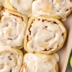 Close-up of soft apple cinnamon rolls covered with creamy maple icing beside a green apple.