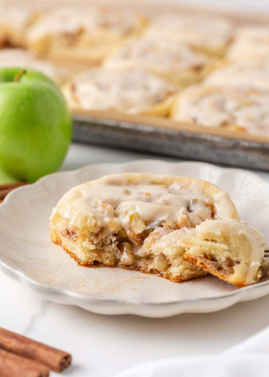 Apple cinnamon roll with maple icing cut open on a plate to show the soft dough, cinnamon filling and diced apples.