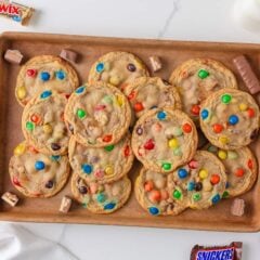 Freshly baked candy cookies with M&M’s and chocolate candy pieces arranged on a baking tray.