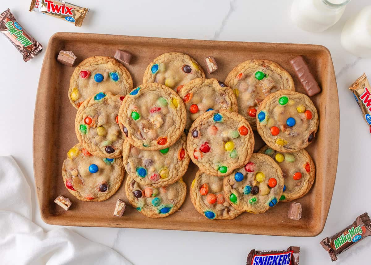 Freshly baked candy cookies with M&M’s and chocolate candy pieces arranged on a baking tray.