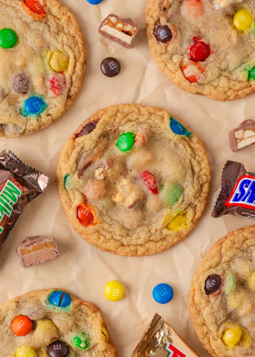 Soft baked candy cookies loaded with colorful M&M’s and chopped candy bar pieces on parchment paper.