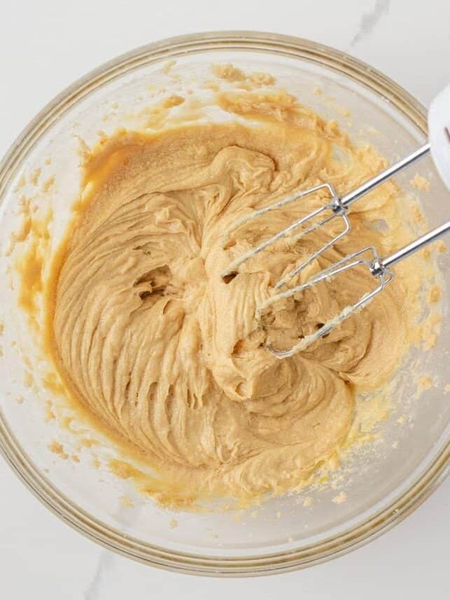 Creamed butter and sugar mixture in a glass bowl with an electric hand mixer.