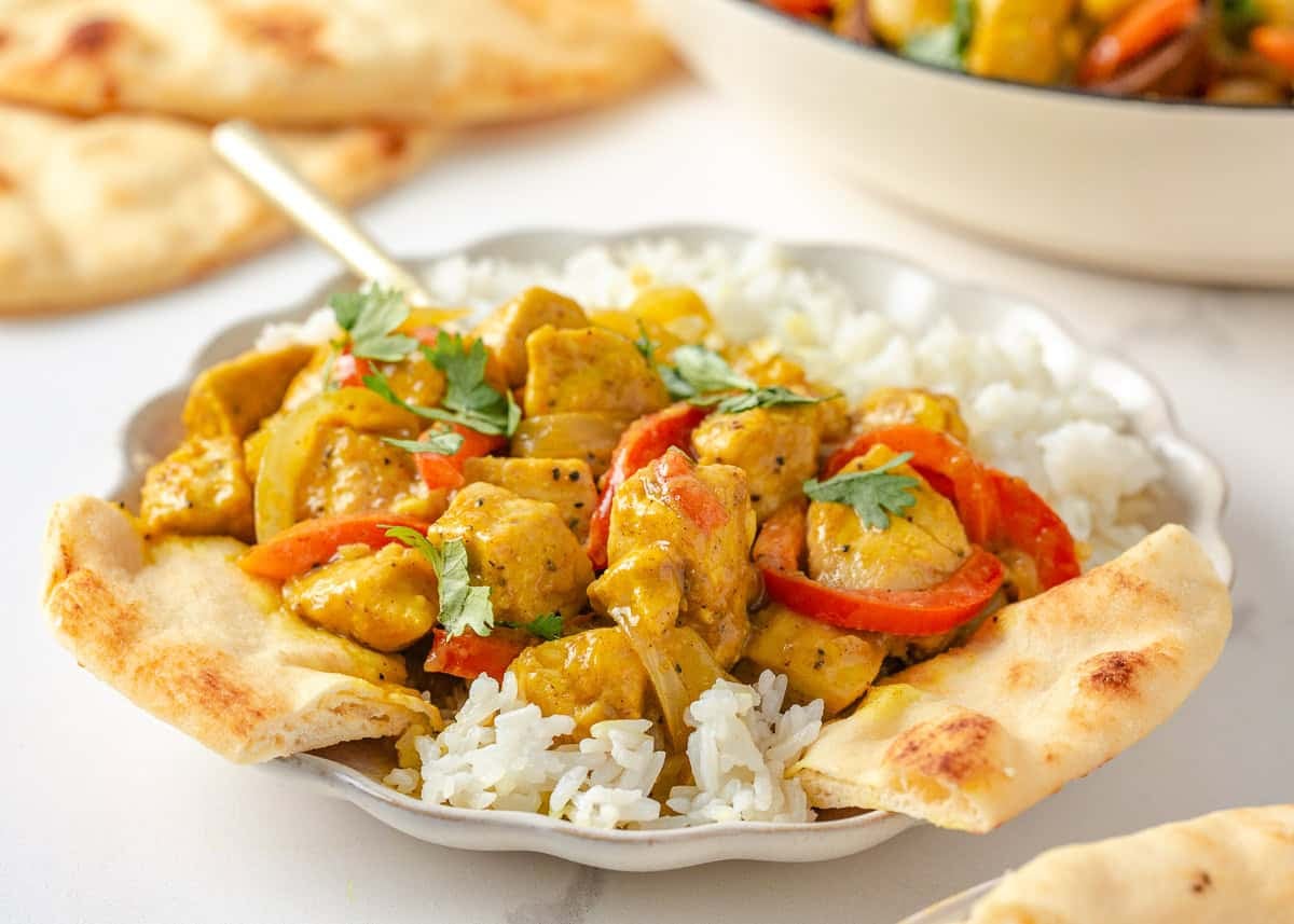 Coconut curry chicken served over white rice with naan and fresh cilantro.