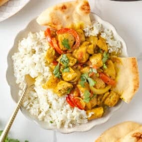 Creamy coconut curry chicken with peppers and onions served with white rice and warm naan.