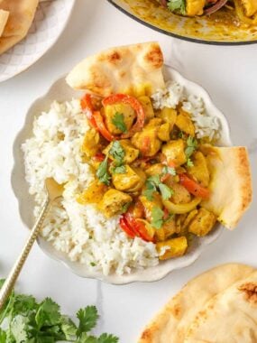 Creamy coconut curry chicken with peppers and onions served with white rice and warm naan.
