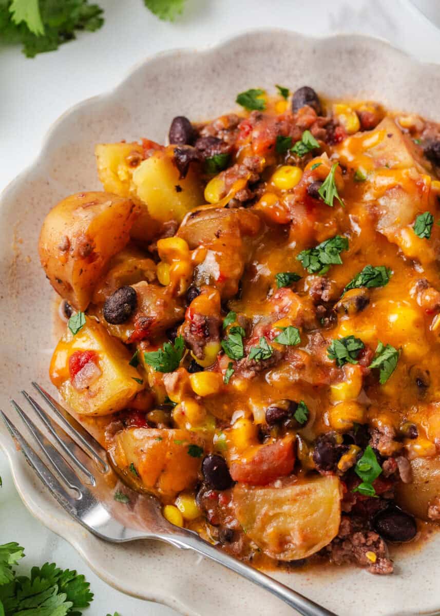 Crockpot cowboy casserole with ground beef, potatoes, black beans, corn and melted cheddar cheese served on a plate.