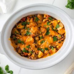 Crockpot cowboy casserole topped with melted cheddar cheese and fresh cilantro in a slow cooker.