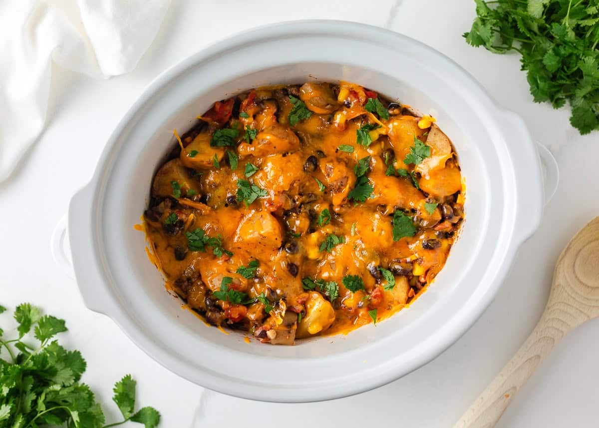 Crockpot cowboy casserole topped with melted cheddar cheese and fresh cilantro in a slow cooker.