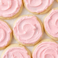 Copycat Crumbl sugar cookies with swirls of pink frosting arranged on parchment paper.