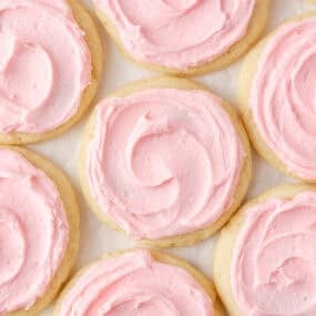 Overhead view of soft Crumbl sugar cookies topped with thick pink almond frosting.