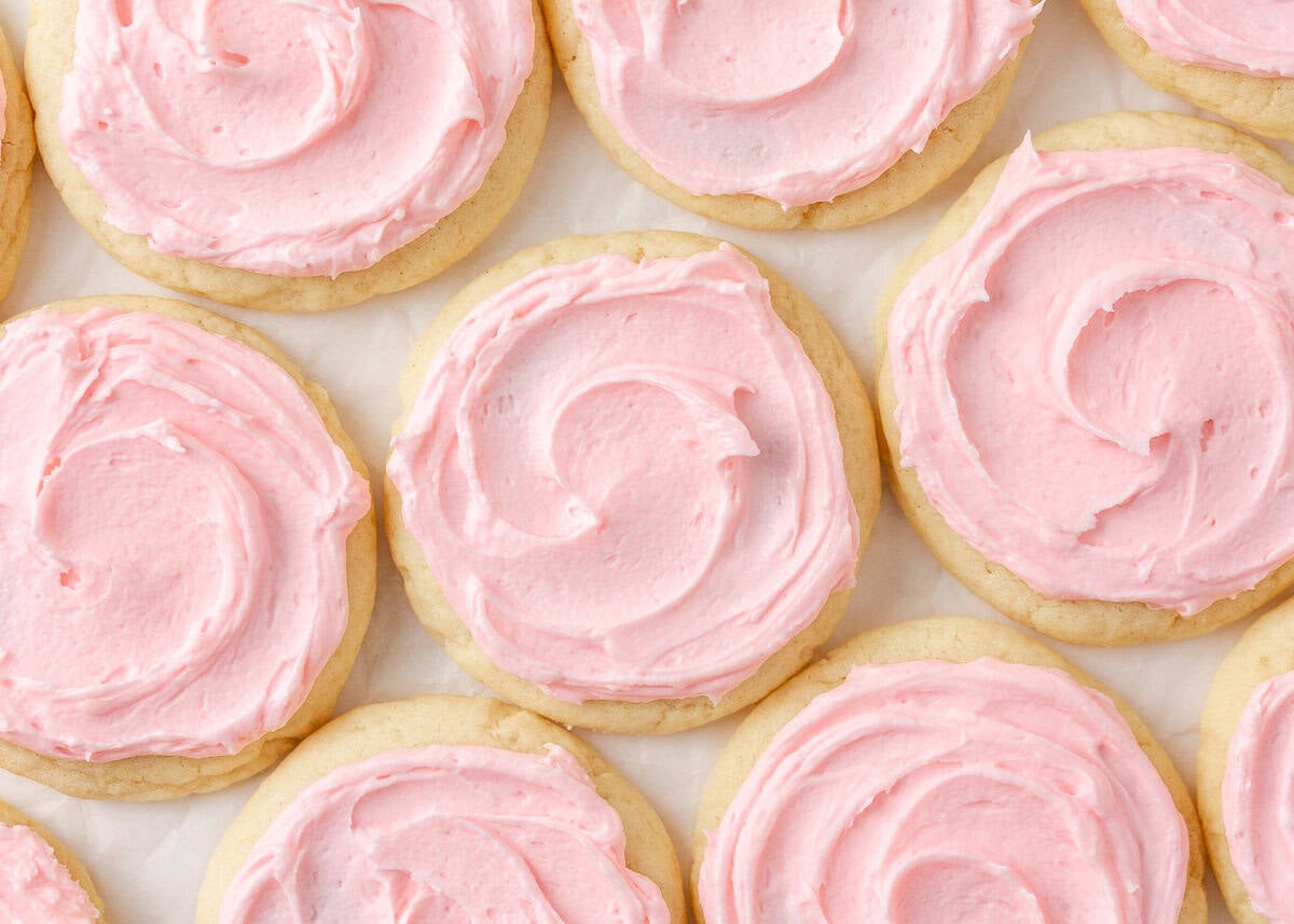 Copycat Crumbl sugar cookies with swirls of pink frosting arranged on parchment paper.