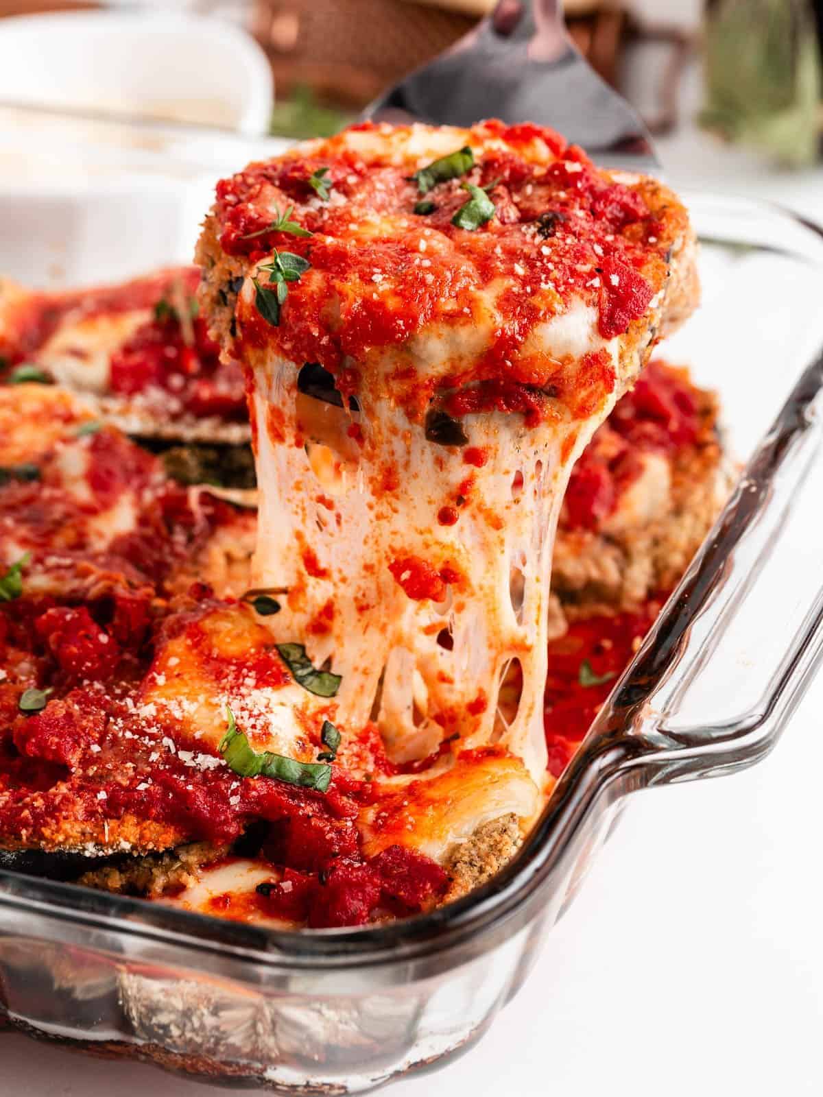Pulling eggplant parmesan out of baking dish.