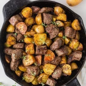 Garlic butter steak and potatoes with browned steak bites, golden potatoes and fresh thyme in a cast iron skillet.