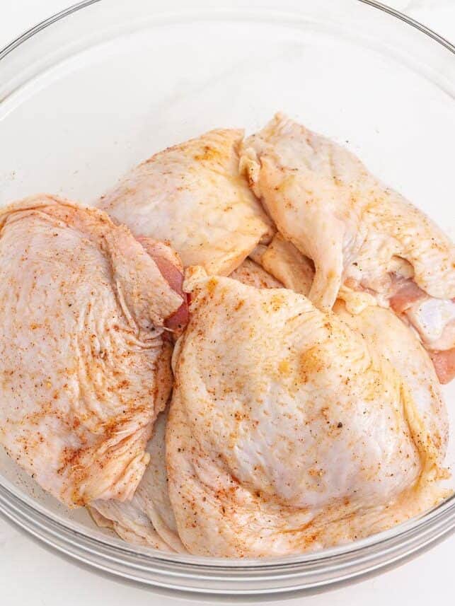 Raw chicken thighs in a bowl with dry rub on it.