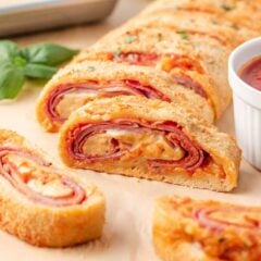 Close-up of sliced stromboli with layers of ham, pepperoni and melted cheese served with pizza sauce.