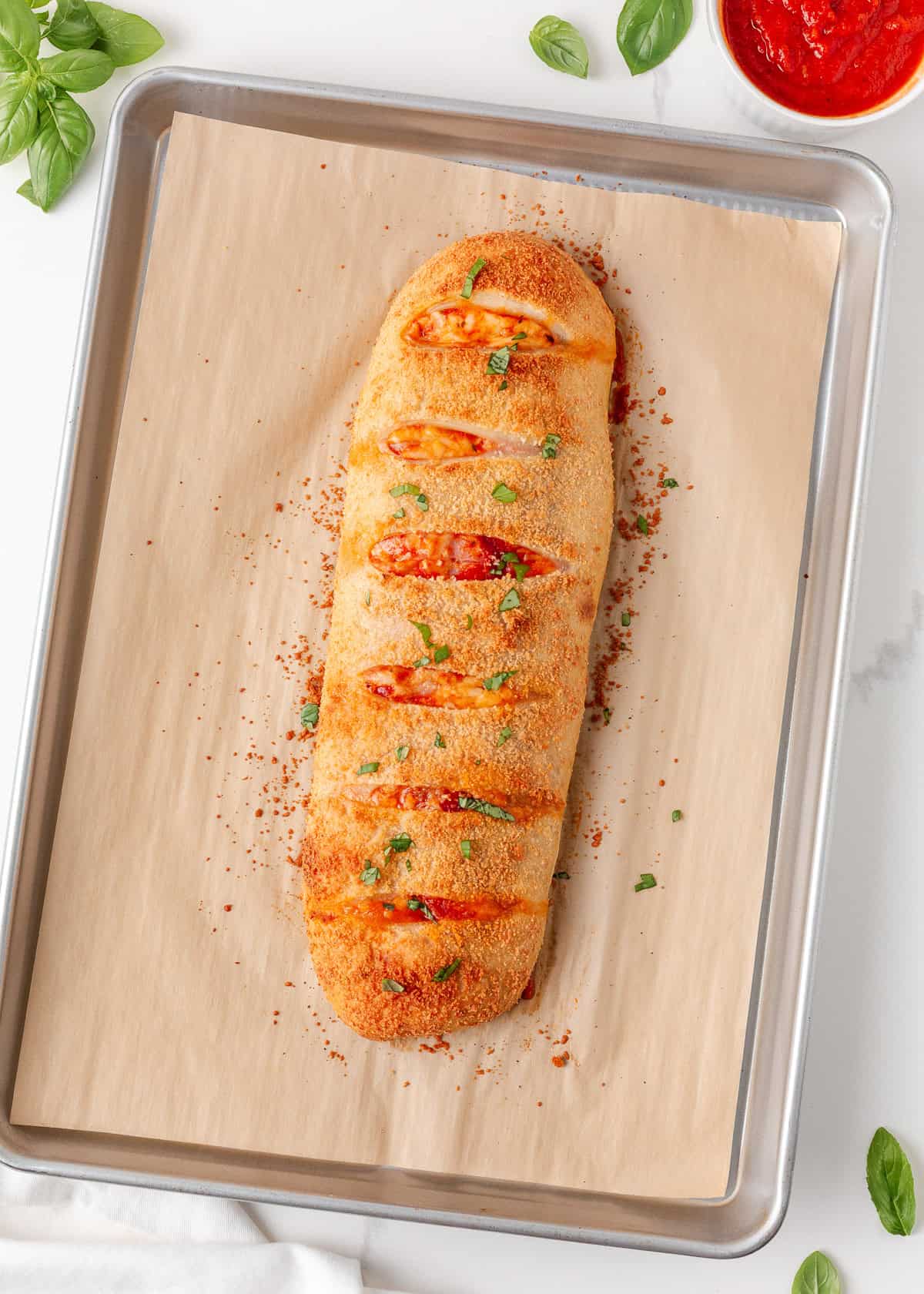 Whole baked stromboli with a golden Parmesan crust and melted cheese showing through the slits.