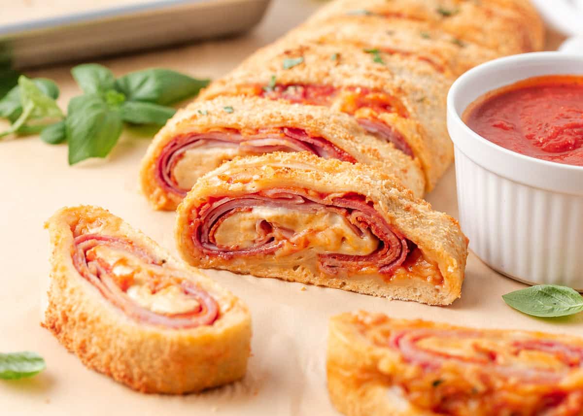 Close-up of sliced stromboli with layers of ham, pepperoni and melted cheese served with pizza sauce.
