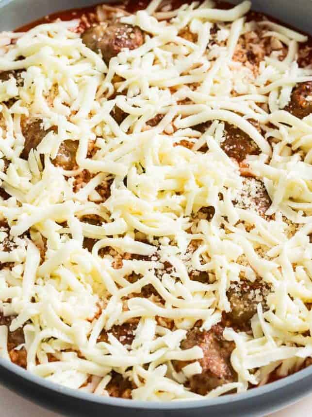 Cheese covering meatballs in a skillet.