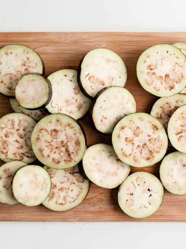 Salted slices of eggplant sweating on a cutting board.