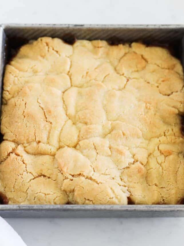 Baked apple cobbler with a golden cracked topping in a square metal pan.
