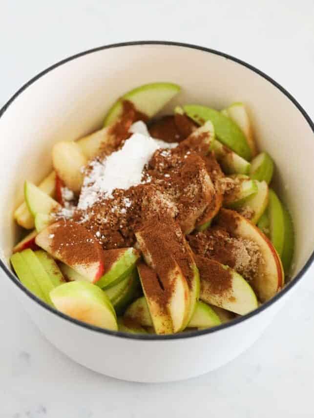 Sliced apples in a white pot topped with cinnamon, brown sugar, and cornstarch.