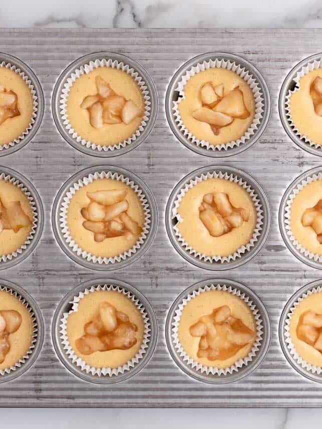 Cupcake batter in muffin tin with apple filling for apple pie cupcakes.