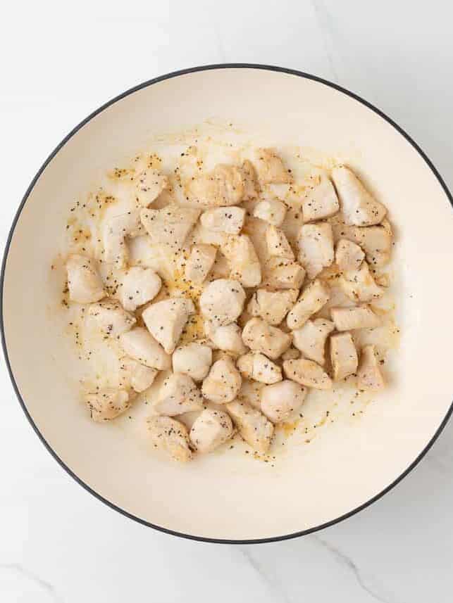 Cooking chicken in a white skillet for chicken and apples.