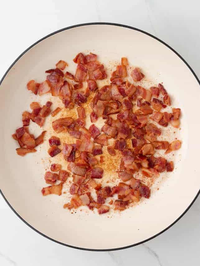 Cooking bacon in a white skillet.