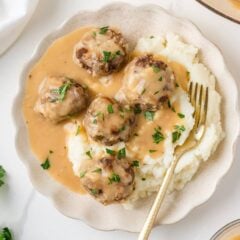 Meatballs and gravy served over creamy mashed potatoes and garnished with fresh parsley.