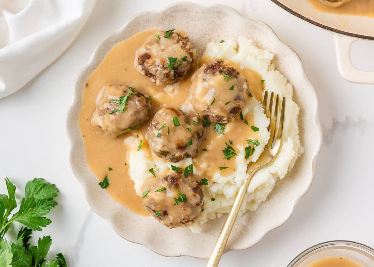 Meatballs and gravy served over creamy mashed potatoes and garnished with fresh parsley.