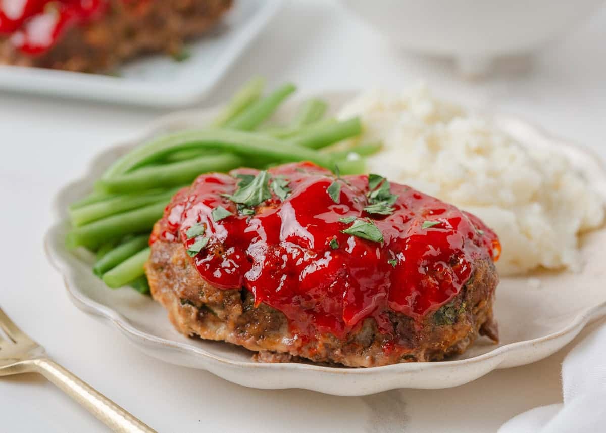 Mini meatloaf on a plate with mashed potatoes and green beans.