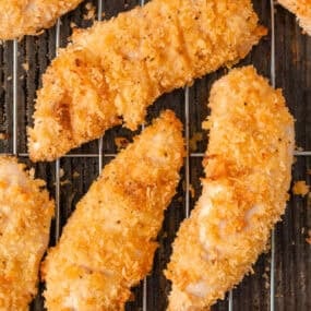 Close-up of golden crispy baked chicken tenders on a wire cooling rack.
