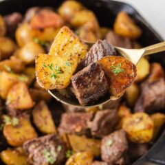 Spoonful of garlic butter steak bites and golden potatoes held over a cast iron skillet.
