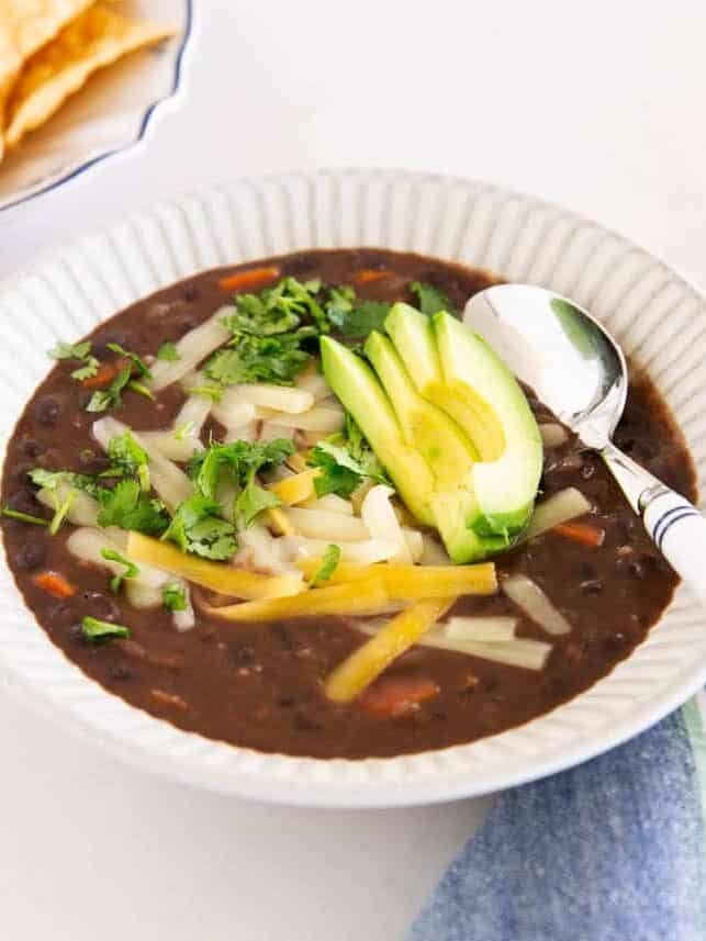 Close-up of black bean soup topped with avocado, cilantro, cheese and tortilla chips to the side.