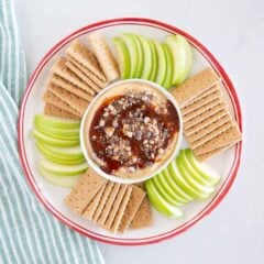 Caramel apple cheesecake dip on a platter surrounded by green apple slices and graham crackers.