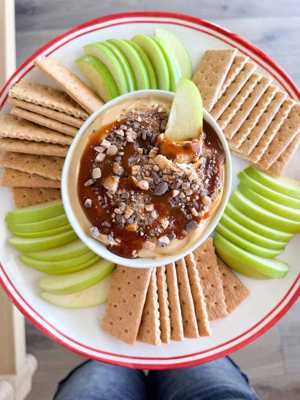 Caramel apple cheesecake dip topped with caramel and toffee bits, served with sliced green apples and graham crackers.