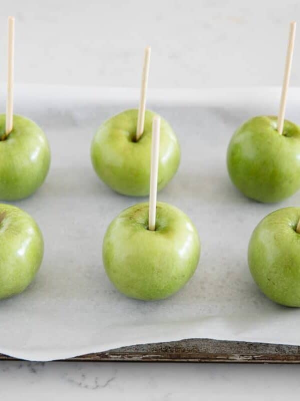 Washed apples resting on a parchment paper lined pan waiting to be dipped in caramel.