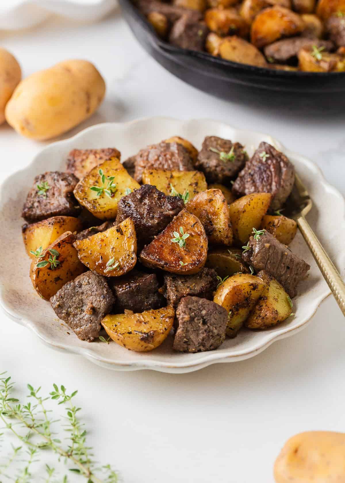 This garlic butter steak and potatoes recipe is made in the skillet for an easy 30 minute weeknight dinner. Exploding with flavor, juicy pan-seared steak and crispy potatoes are a one pan wonder! Garlic butter steak bites and golden potatoes served with fresh thyme, with the skillet in the background.