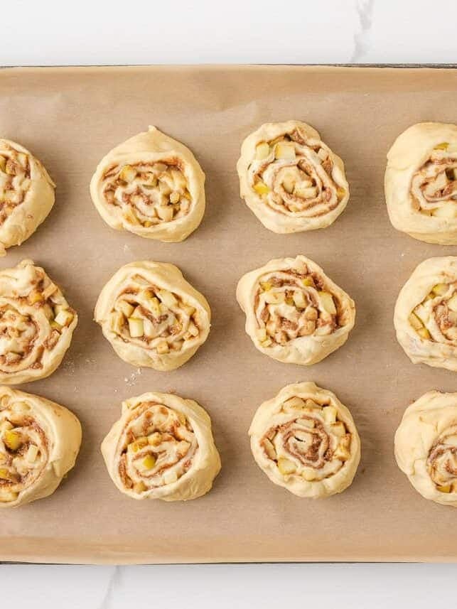 Unbaked apple cinnamon rolls arranged on a parchment-lined baking sheet before rising.