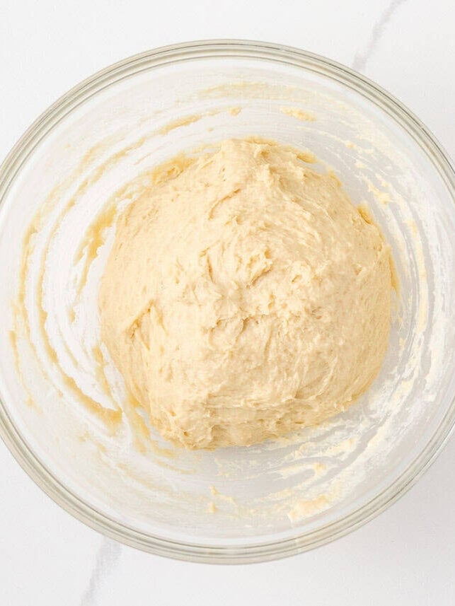 Soft cinnamon roll dough rising in a large glass mixing bowl.