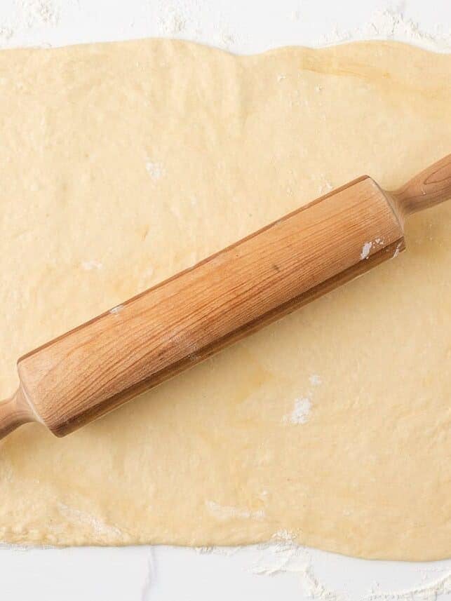 Cinnamon roll dough rolled into a large rectangle with a wooden rolling pin.