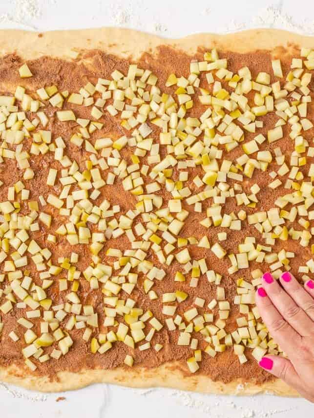 Cinnamon filling and diced green apples spread over rolled-out dough for apple cinnamon rolls.