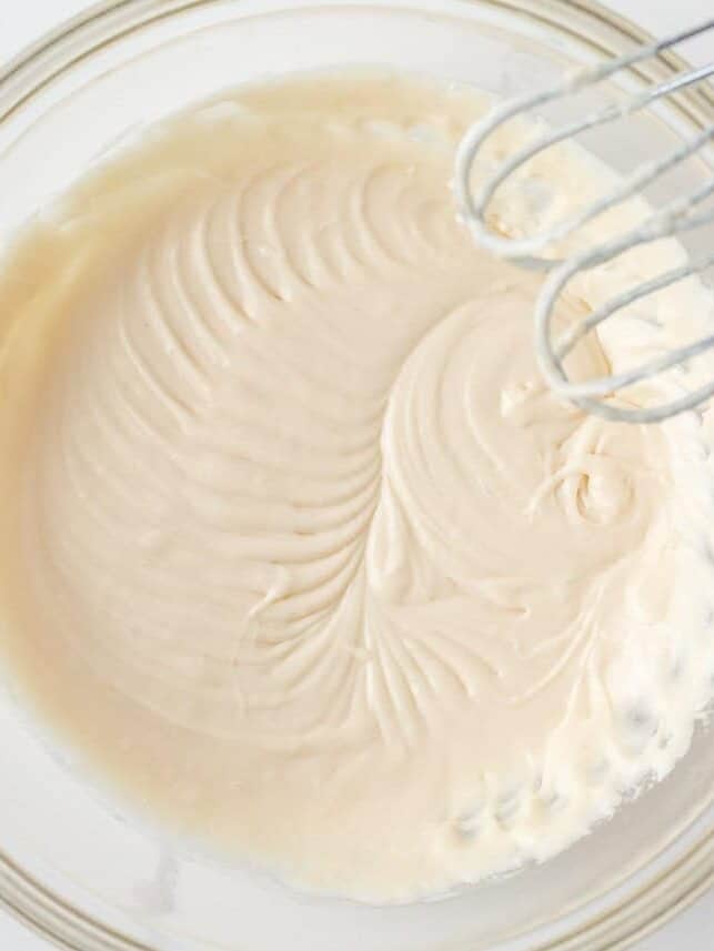 Creamy maple icing being mixed with an electric mixer in a glass bowl.