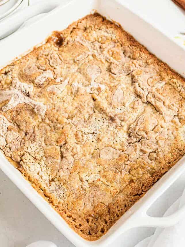 Baked apple dump cake in a white dish with a golden brown cinnamon cake topping.