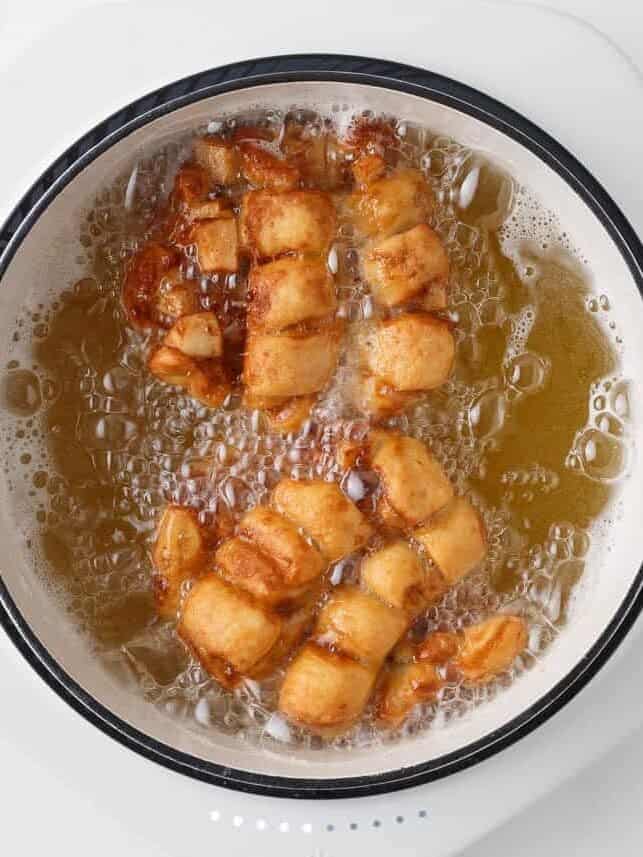 Apple fritters frying in hot oil until golden brown.