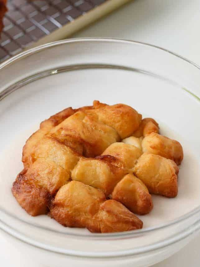Freshly fried apple fritter being dipped in vanilla glaze.