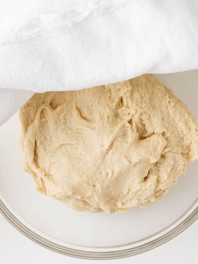 Apple fritter yeast dough rising in a covered glass bowl.
